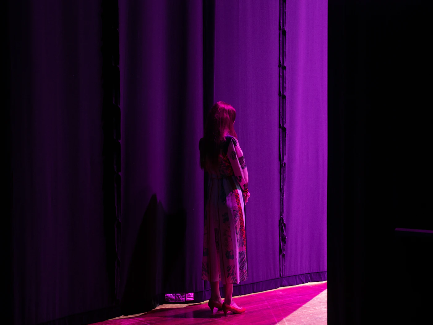 A young performer waiting in the wings beside a purple curtain